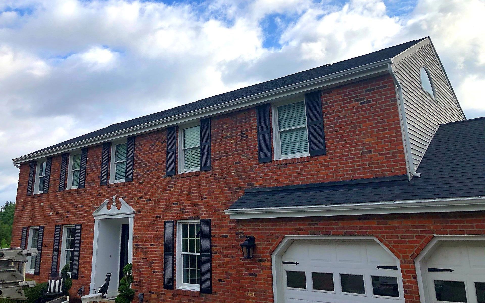 Two-story red brick house with white trim and a double garage under a cloudy sky