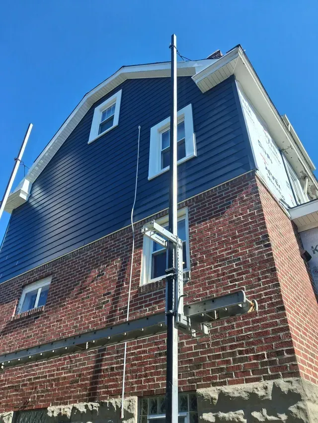 Brick and blue-sided house corner with a tall utility pole against a clear blue sky