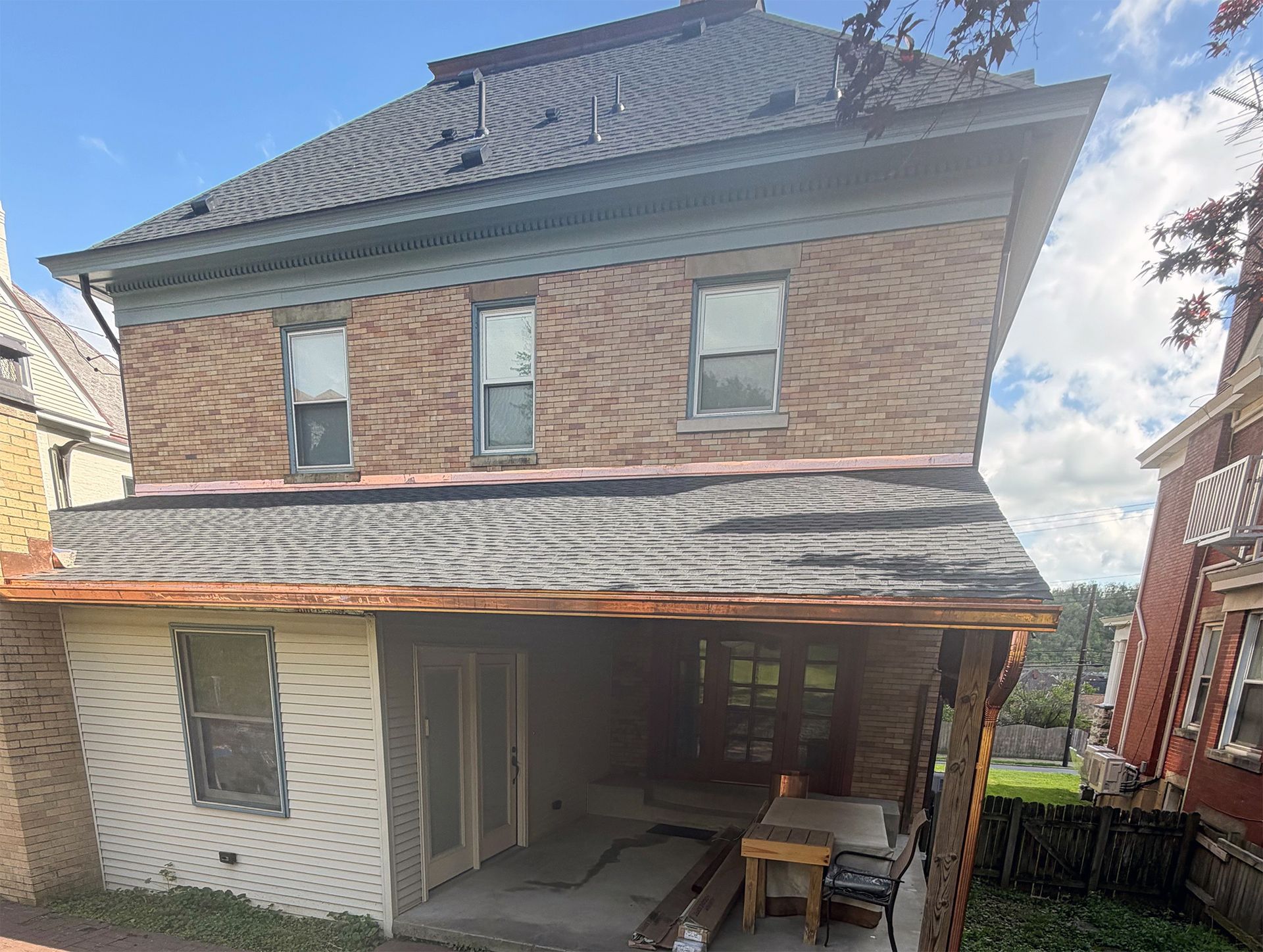 Two-story brick house with a covered porch and small patio table in the backyard