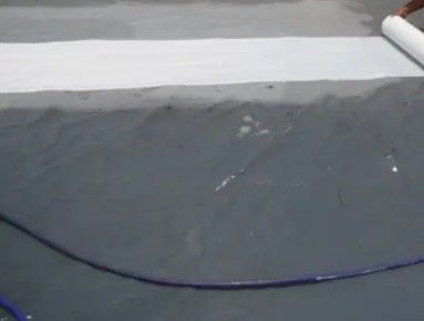 Person rolling out a white waterproof membrane on a gray concrete surface.