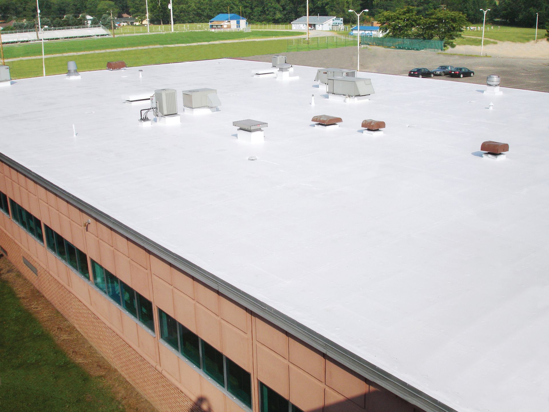 White commercial roof with HVAC units and vents, viewed from above, on a sunny day.
