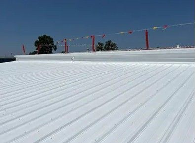 White corrugated metal roof with red poles holding colorful string lights. Clear blue sky.