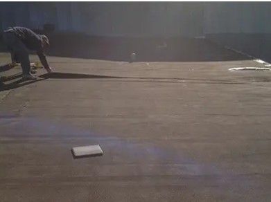 Person placing a base on a dark, flat surface. Sunlit, with shadows.