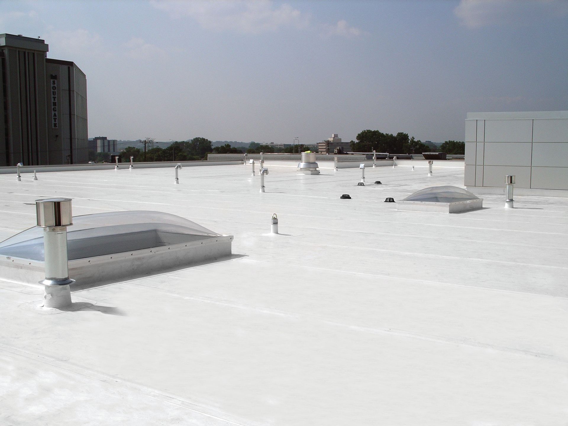 White commercial roof with skylights, vents, and cityscape in the background.
