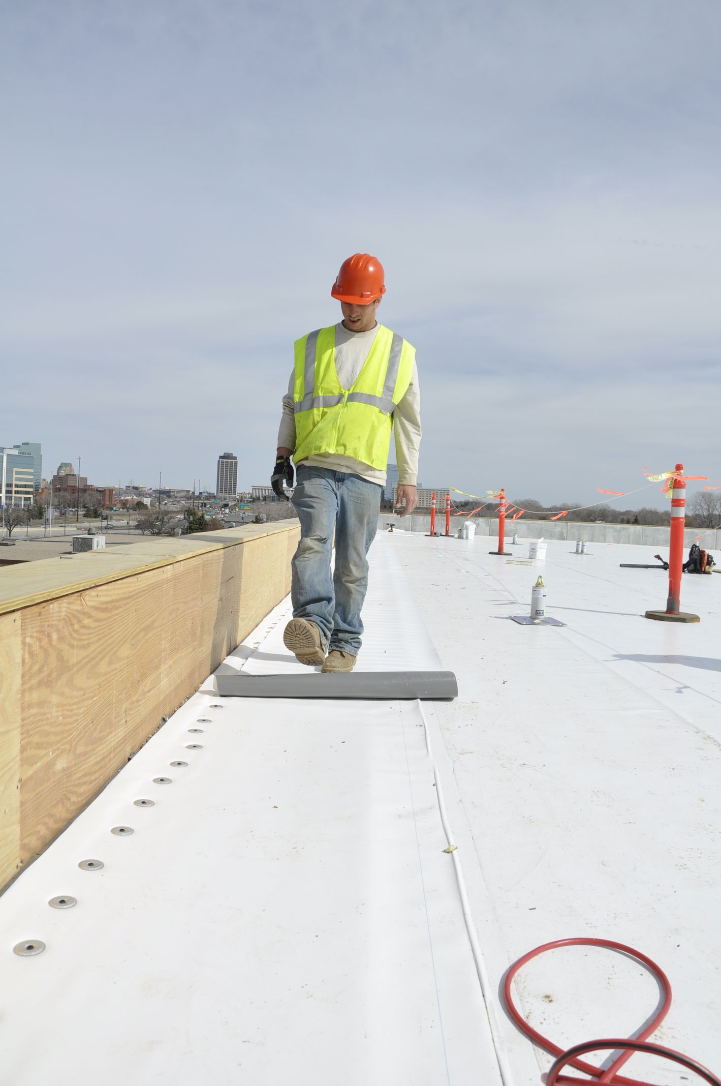 Construction worker in orange hard hat and yellow vest walking on a white rooftop.