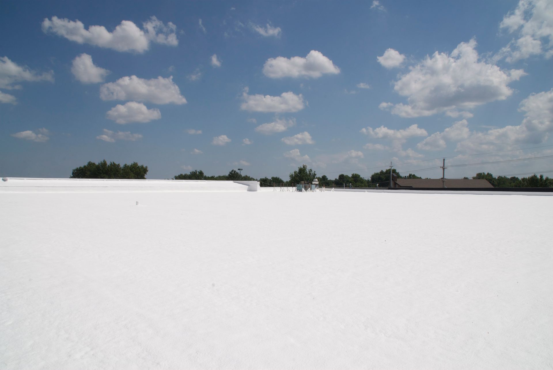 White roof with small trees and buildings against a blue sky dotted with puffy clouds.