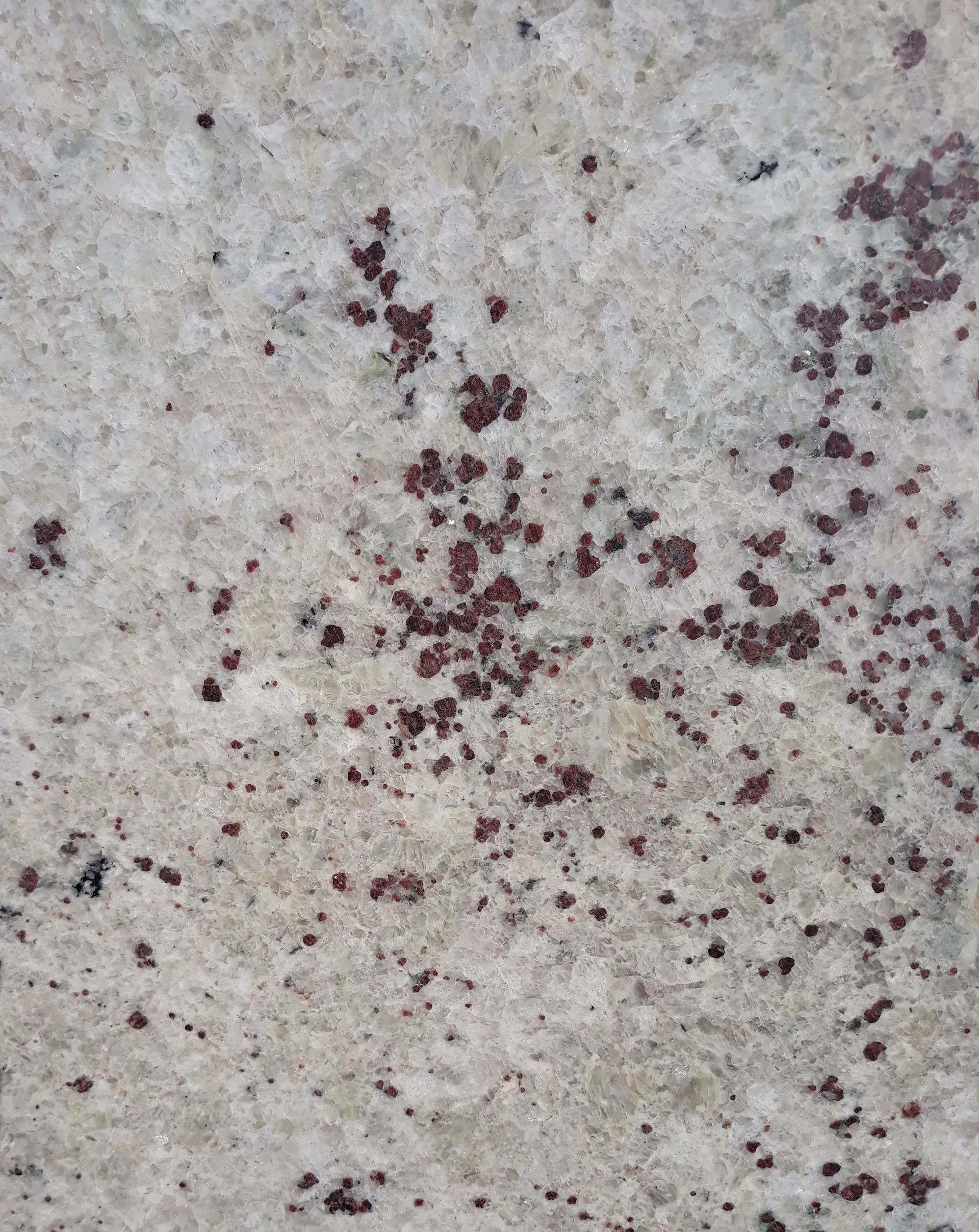 Close-up of a speckled light gray stone surface with scattered dark red stains
