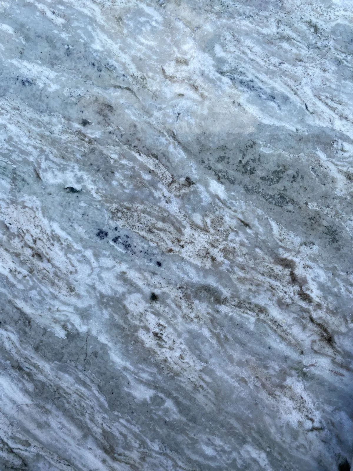 Close-up of light gray and blue marbled stone with dark speckles and streaks