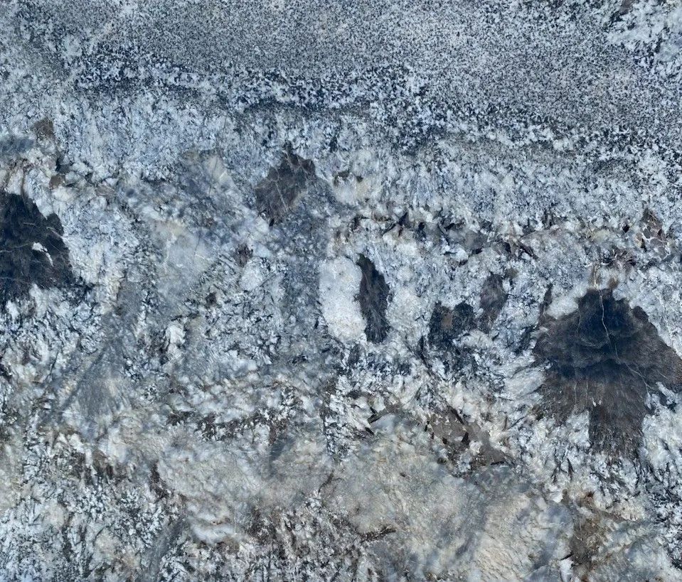 Close-up of gray and white rocky ground with rough, icy-looking texture and dark patches