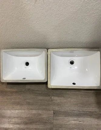 Two white rectangular bathroom sinks sitting side by side against a wall on wood flooring.