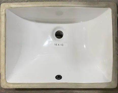 White bathroom sink basin with a central drain hole and overflow opening, shown from above.