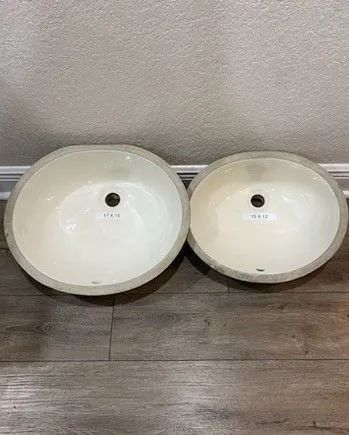 Two white round vessel sinks on a wood floor against a light wall.