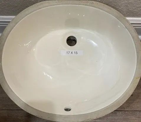 White oval bathroom sink basin with a center drain hole and a small label reading “17 x 15”