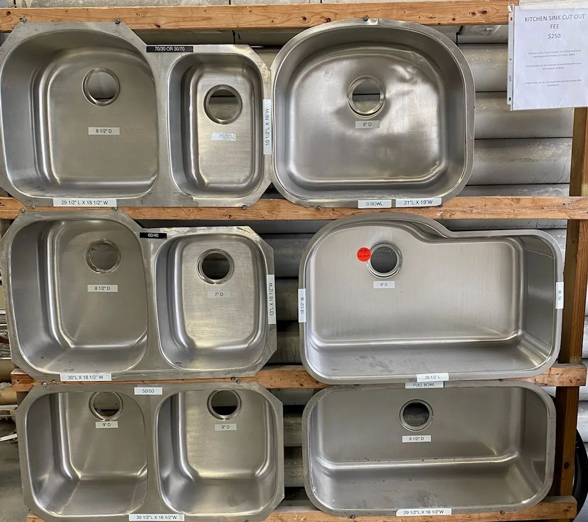 Stacked stainless steel sinks displayed on wooden shelves in a store or warehouse.
