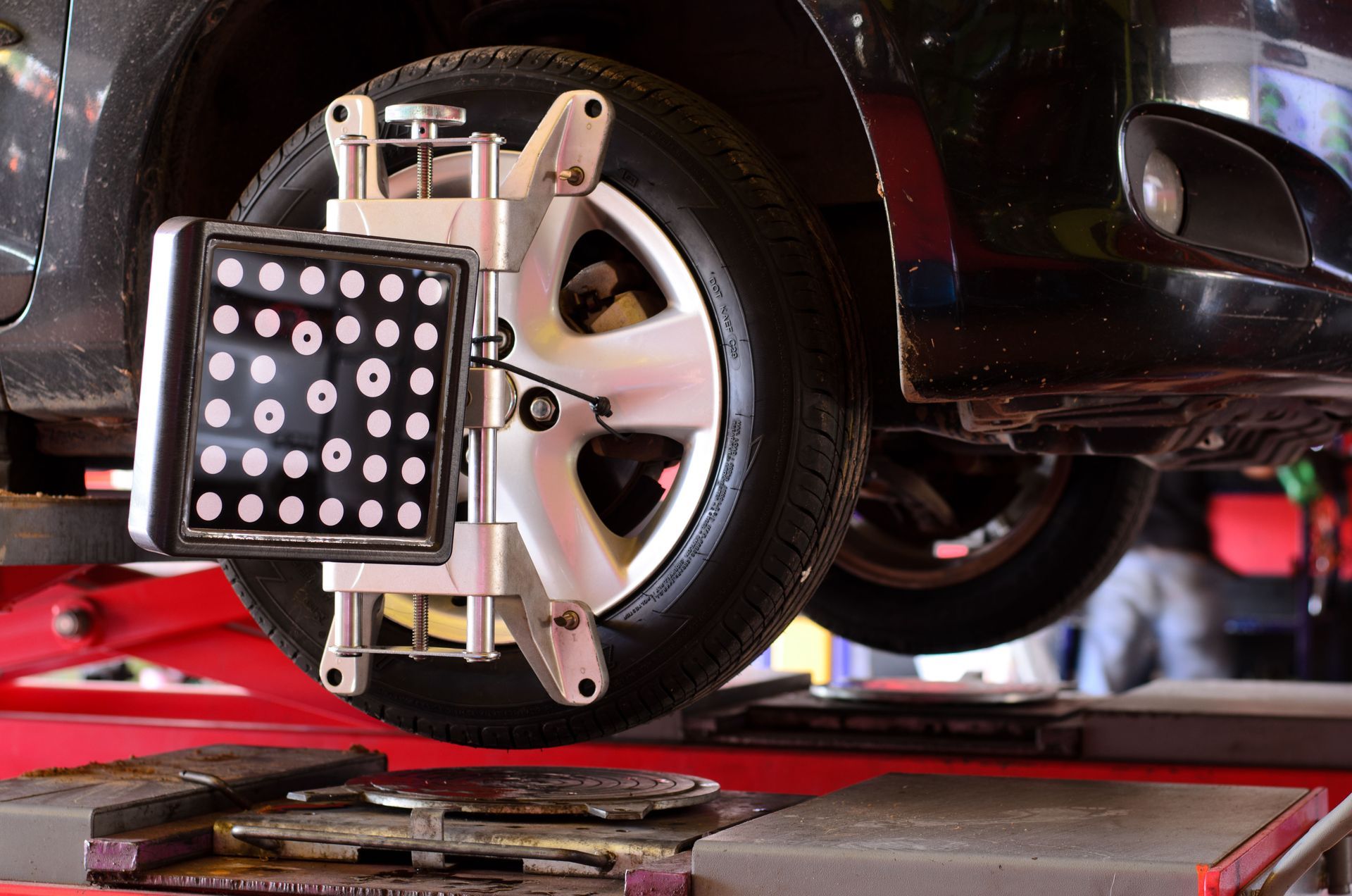 Car tire being aligned on a lift, using a wheel alignment machine with sensors.