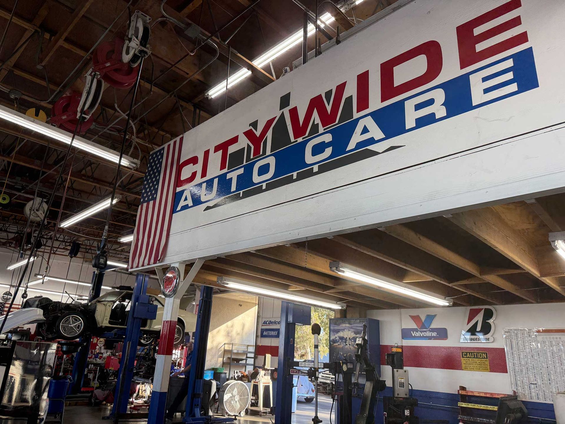 City Wide Auto Care sign in a garage with a U.S. flag. Cars on lifts, tools, and equipment are visible.