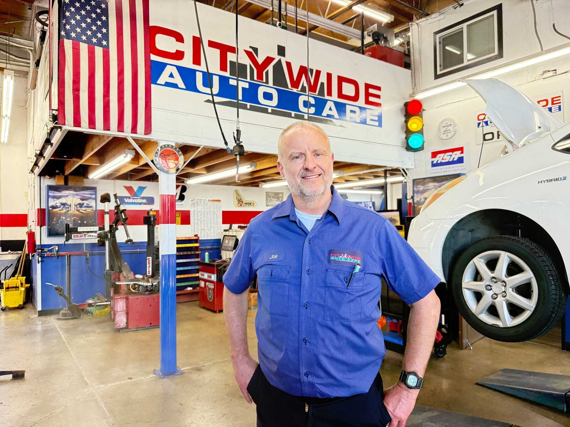 Man in auto shop stands in front of a raised car.