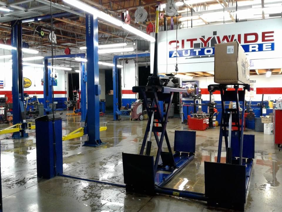 Inside a Citywide Auto Care shop, a vehicle is on a blue lift. A box sits on a platform.