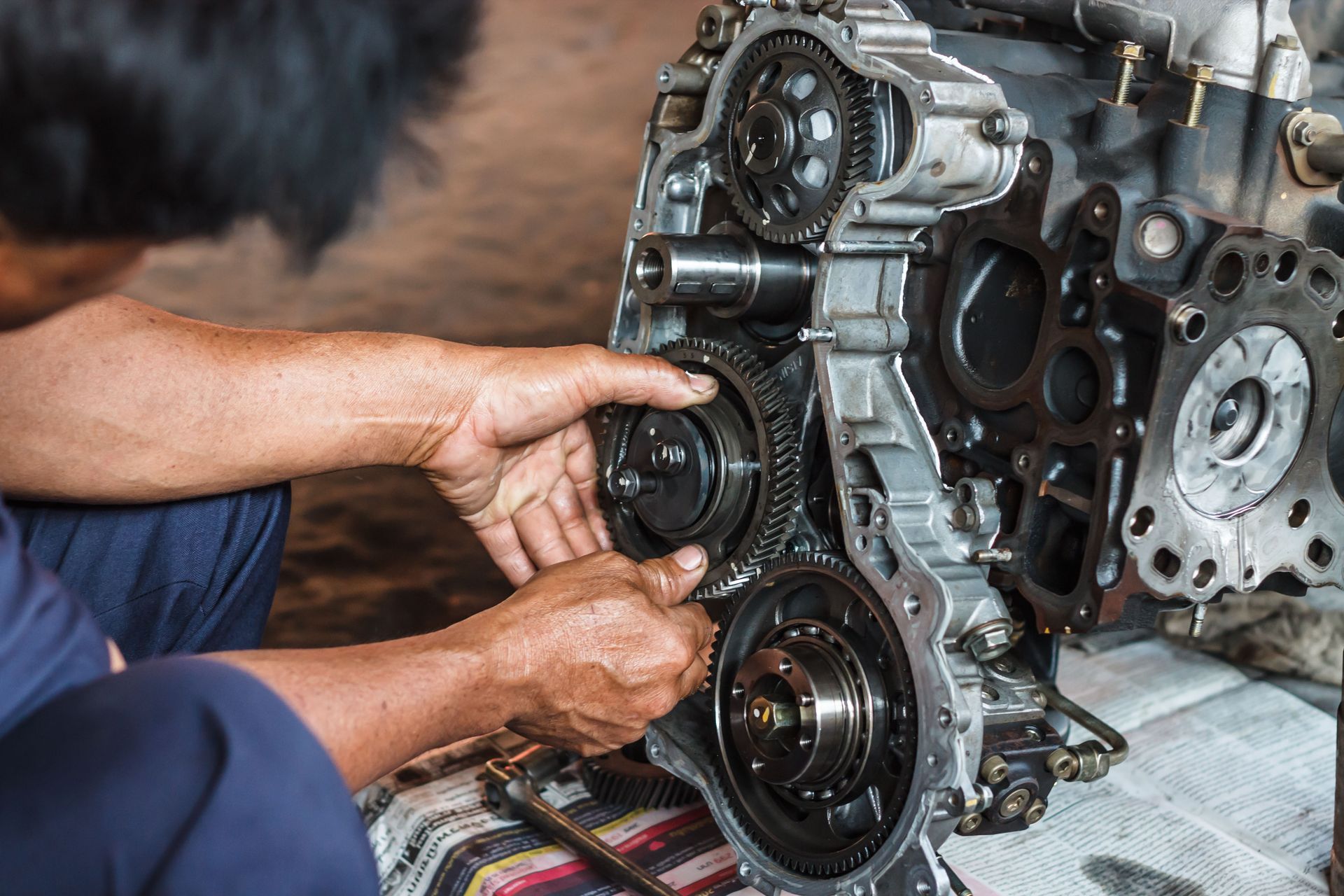 Mechanic's hands assembling engine components; gears, metal parts; repair in progress.