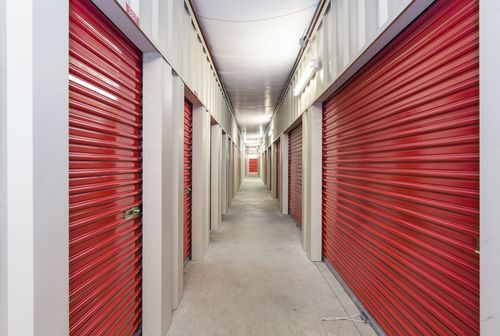 Narrow storage hallway with red roll-up doors on both sides and a concrete floor