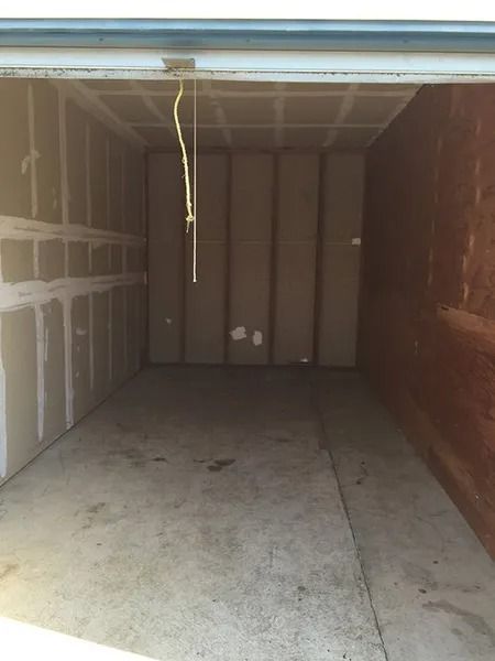 Empty unfinished garage with bare drywall, concrete floor, and a hanging cord from the ceiling.