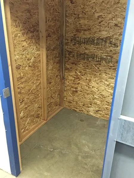 Empty unfinished room with OSB plywood walls and a concrete floor, viewed through an open doorway