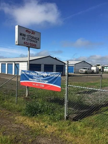 Storage facility with chain-link fence, blue sign, and red-white-blue banner under a partly cloudy sky