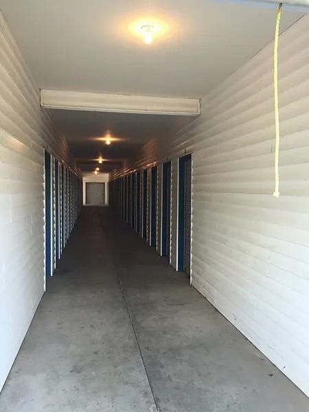 Long, narrow apartment hallway with white walls, concrete floor, and overhead lights.