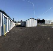 Row of blue-and-white storage units with a paved driveway under a clear sky