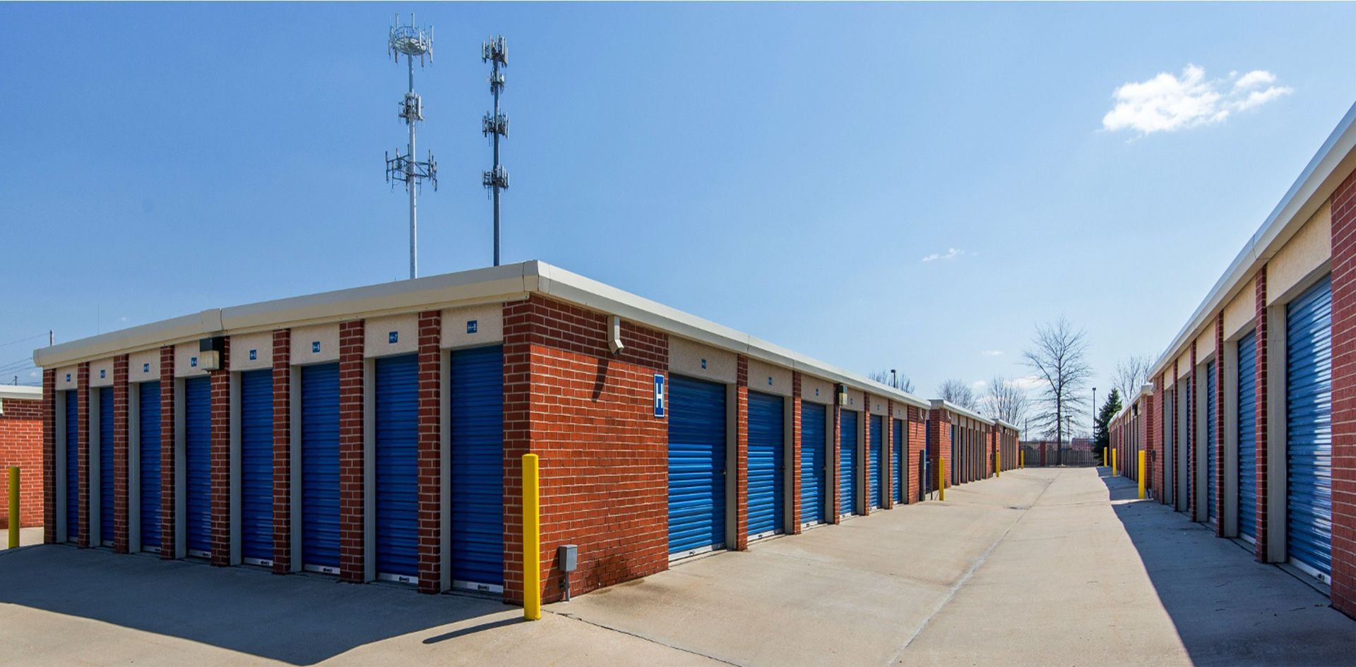 Storage unit row with blue doors beside a paved drive under a clear sky
