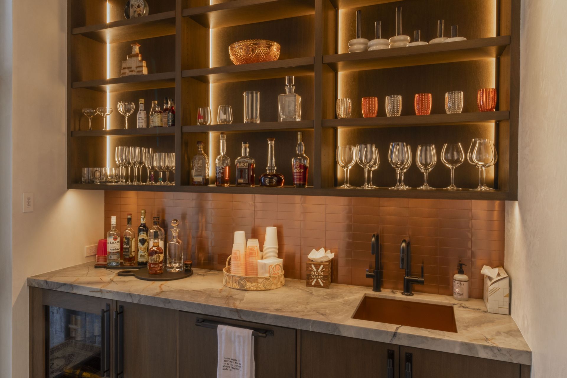 A bar with a sink, shelves, bottles, and glasses on it