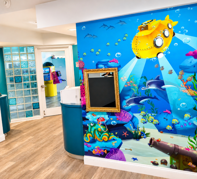 Child’s playroom with desks, toys, stuffed animals, colorful wall art, and a blue cabinet.