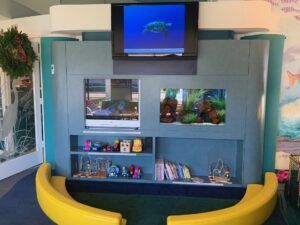 Aquarium-themed display with fish tank, TV, shelves of books, and a bright yellow bench seating area.