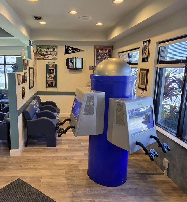Dental office with a blue robot-shaped chair in the waiting room and wall-mounted TVs.