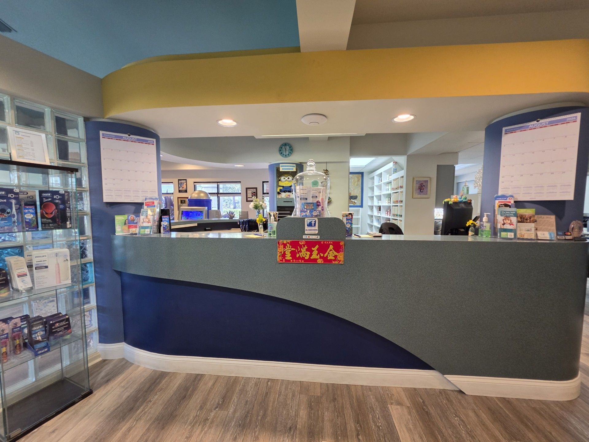 Hospital or clinic reception desk with blue and gray front, brochure racks, and waiting area behind it