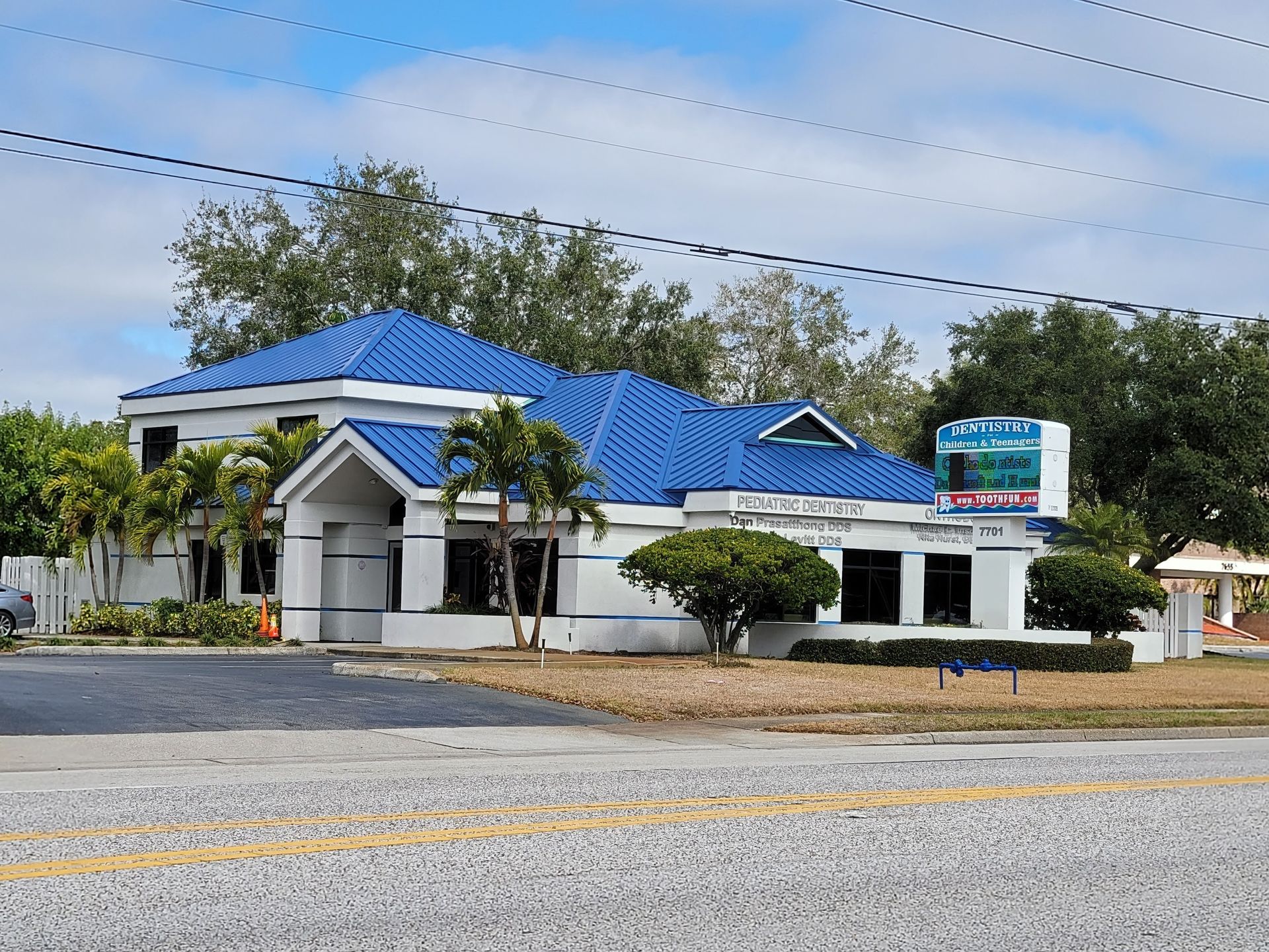Single-story white building with a blue metal roof and roadside sign under a cloudy sky.