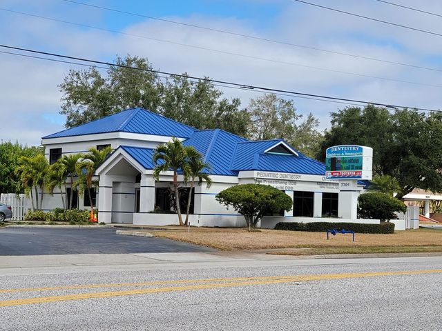 Small white building with a blue roof and sign by a roadside under a cloudy sky