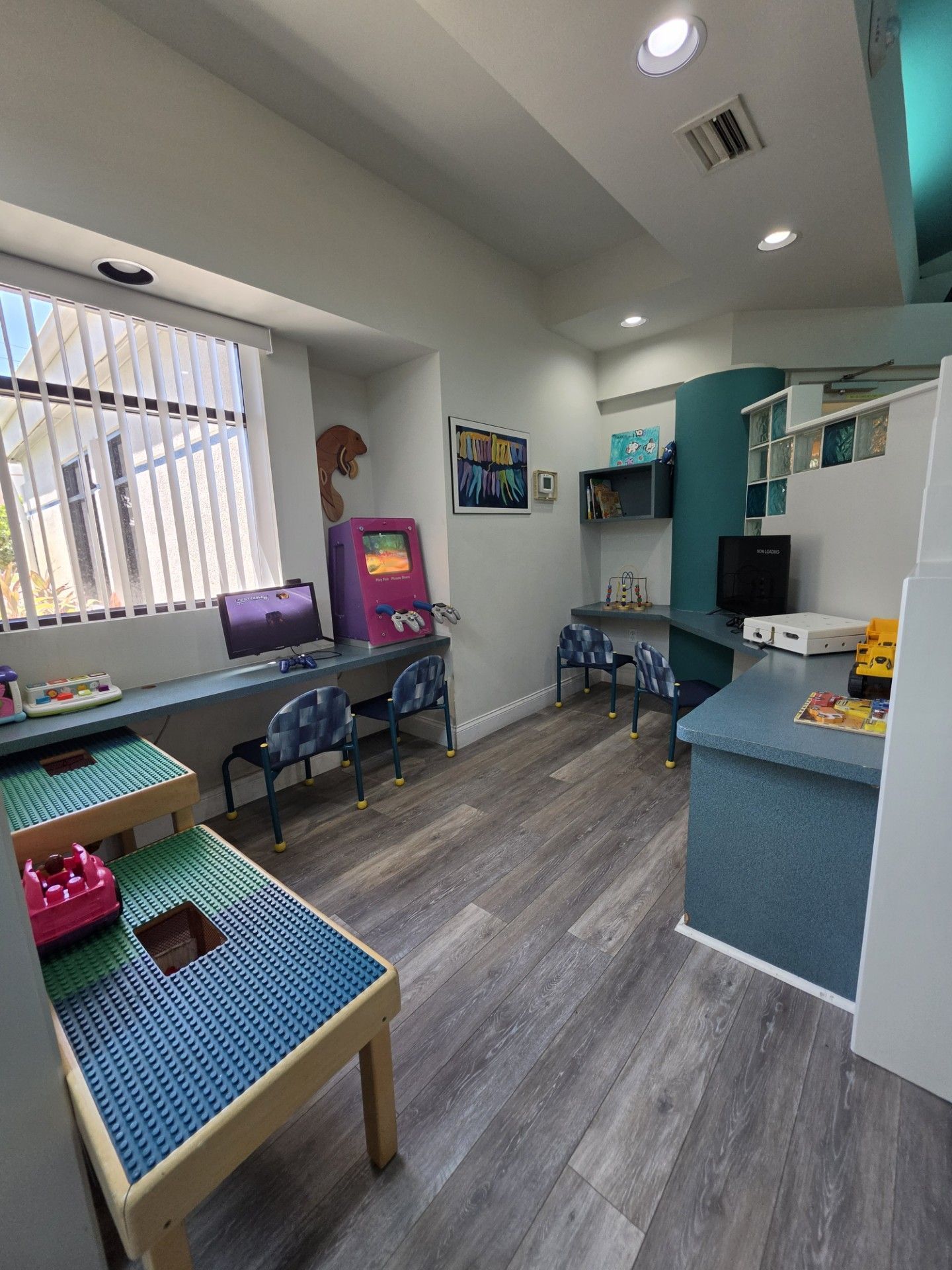 Bright classroom playroom with toys, stuffed animals, small tables, and a computer by the window
