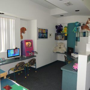 Child’s playroom with desks, toys, stuffed animals, colorful wall art, and a blue cabinet.