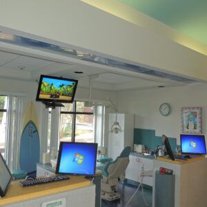 Hospital room with several monitors and medical equipment near windows, a wall clock, and a patient's bed