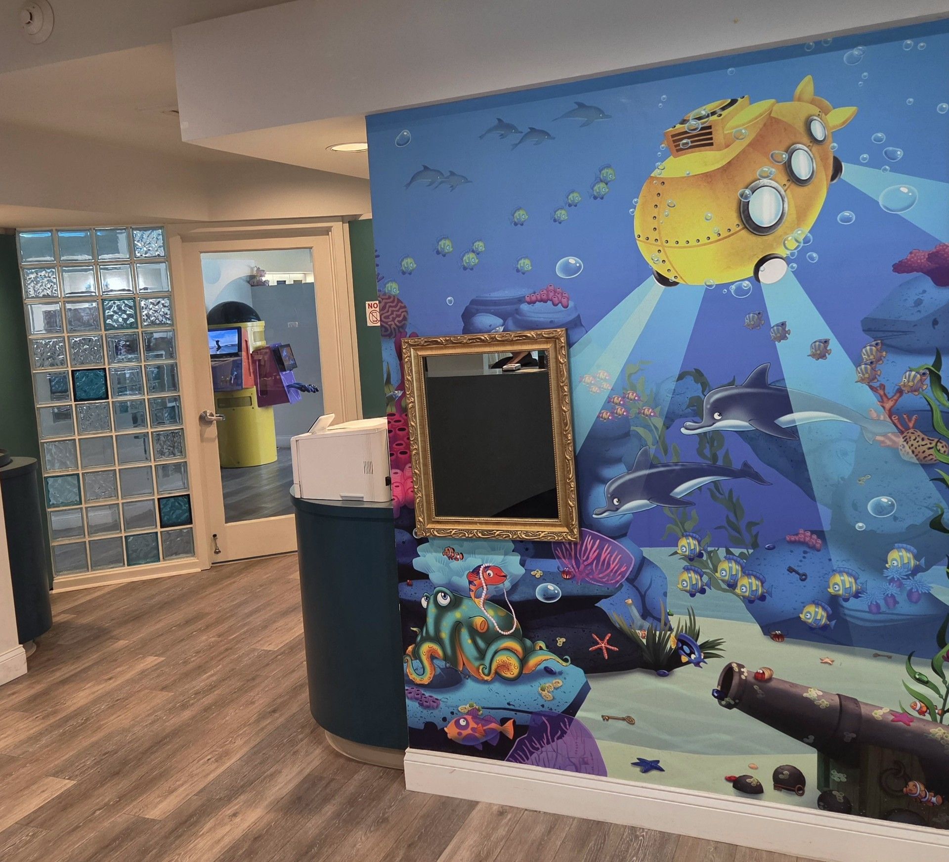 Undersea-themed hallway wall mural with fish, sea creatures, and a framed display near a glass-block doorway