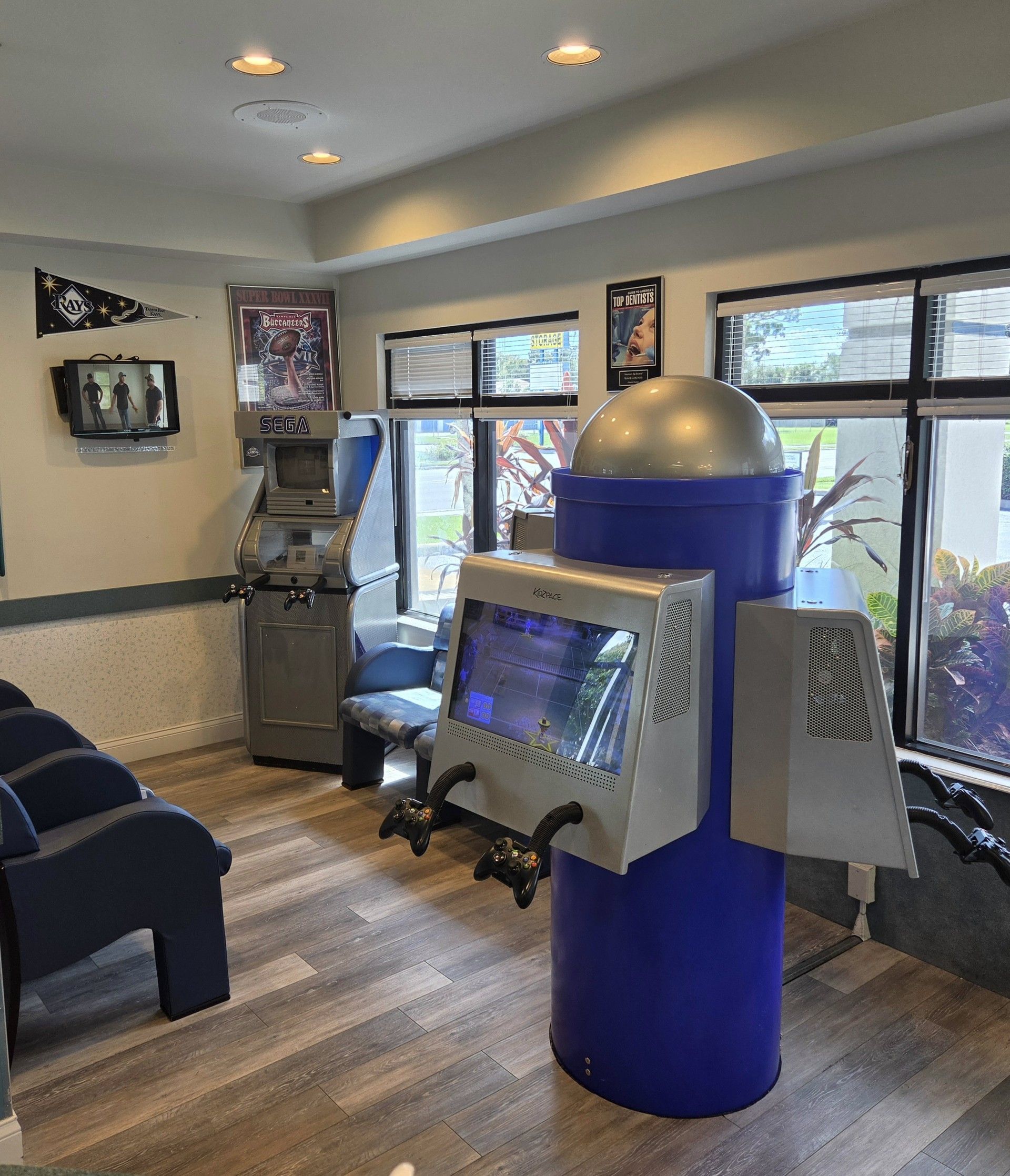 Modern office room with a blue cylindrical kiosk and mounted screens near windows, sofas, and wall art