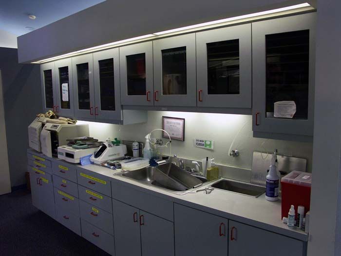 Dental clinic treatment room with cabinets, sink, counter equipment, and overhead lighting