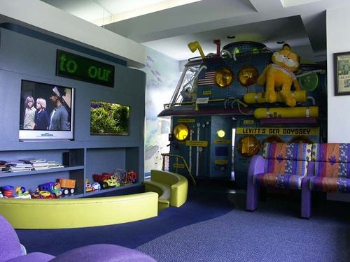 Playful room with a TV, colorful shelves, purple carpet, and a loft bed with stuffed animals
