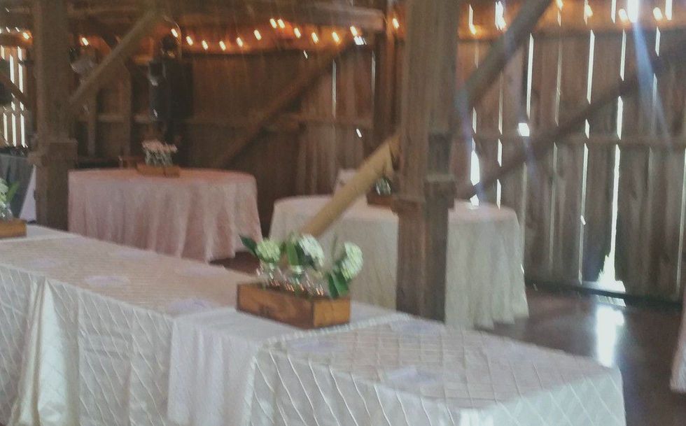 Decorated rustic banquet tables with white linens, candles, and floral centerpieces in a wooden barn setting
