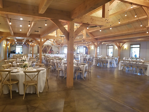 Wooden banquet hall with round tables, white chairs, and exposed beams under warm lighting