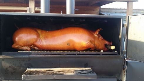 Whole roasted pig on a spit in a smoker, browned and cooking over heat.
