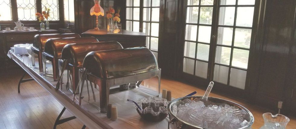 Buffet table with metal chafing dishes and serving trays in a sunlit dining room