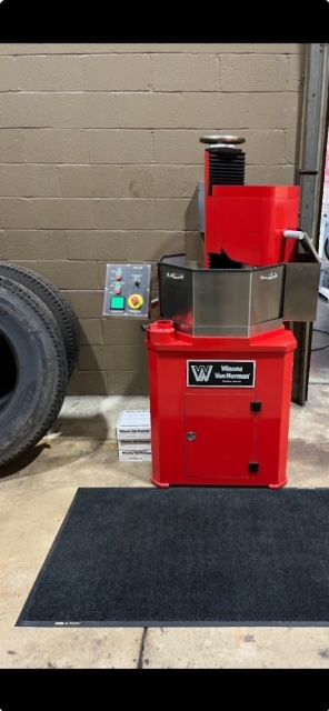A red machine is sitting on the ground next to a tire.