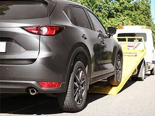 a grey car being towed by a flatbed tow truck on a sunny day